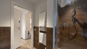 A modern bathroom with a glass shower enclosure, a built-in towel rack, and a visible door leading to another room.