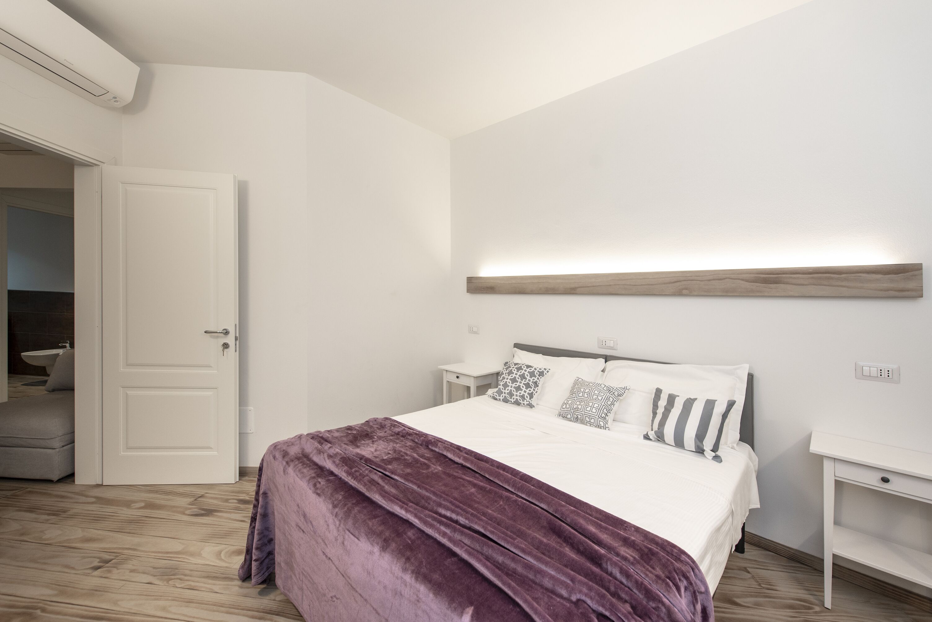 Een slaapkamer met een bed, nachtkastjes, een houten hoofdbord en een witte deur.