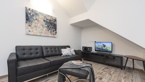 Una sala de estar moderna con un sofá de cuero negro, una mesa de centro, un televisor y una obra de arte geométrica en la pared.