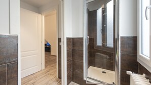 Un baño moderno con ducha de vidrio, bañera blanca y radiador a la vista.