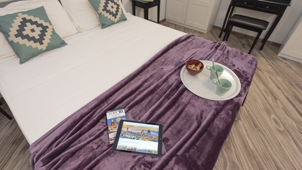 Una cama bien hecha con una manta púrpura, una tableta mostrando una revista y una bandeja con una taza y un platillo.