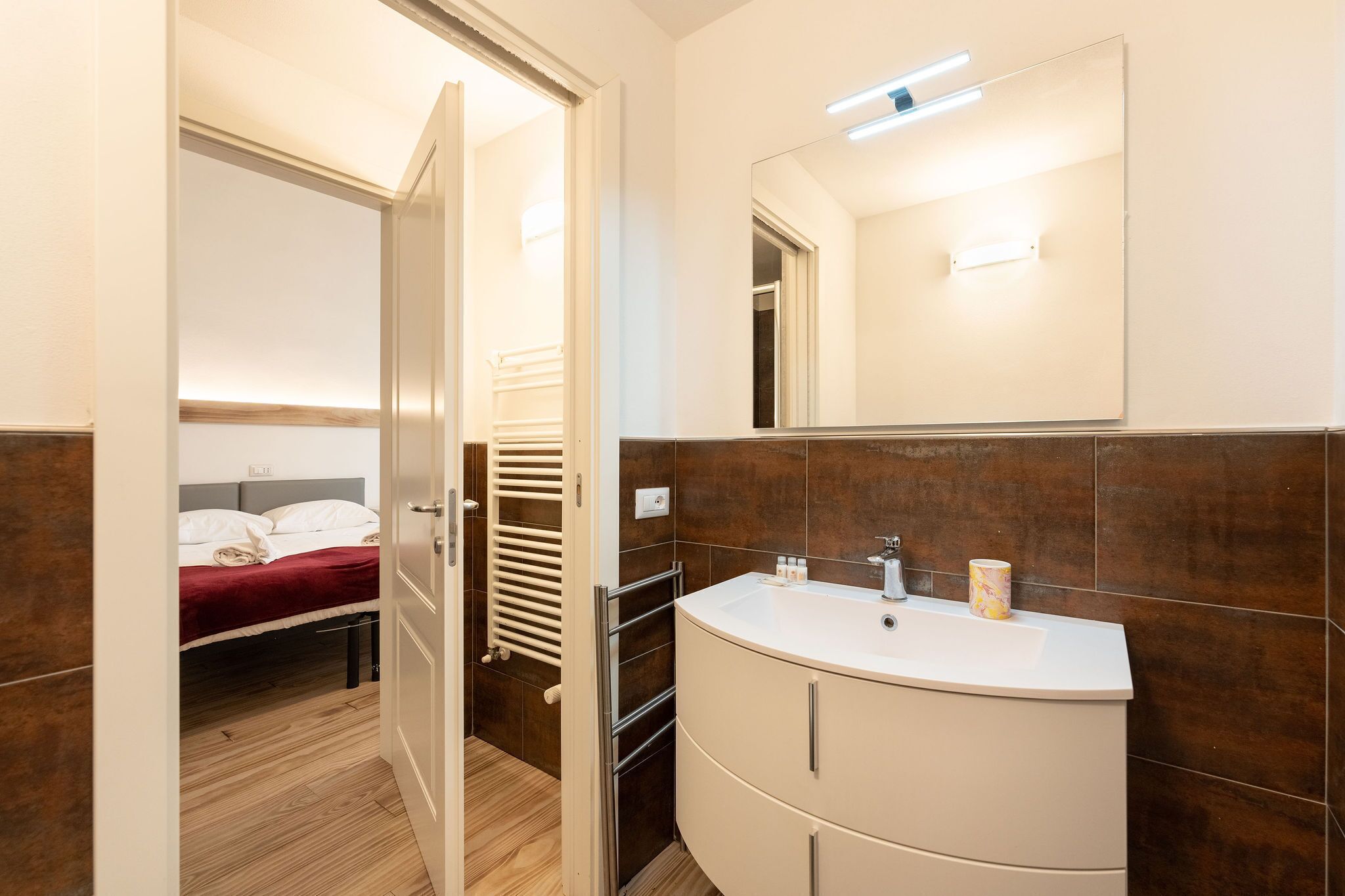 A modern bathroom with a curved white sink, a large mirror, and a towel rack.