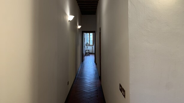 A narrow hallway with white walls, wooden ceiling beams, and a dark wooden floor.