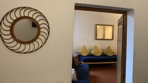 A room with a circular wall decoration, a bed with blue bedding and yellow pillows, and a framed mirror on the wall.
