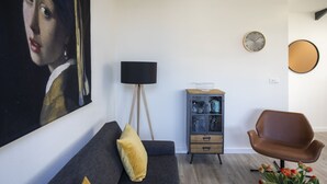 Un soggiorno con un divano scuro, una lampada, un mobile, una poltrona e un quadro appeso al muro.