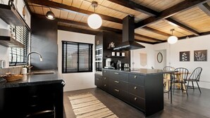 A modern kitchen with a central island, black cabinetry, and a wooden ceiling.