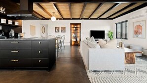 A modern kitchen with dark cabinetry, a central island, and a dining area with chairs.