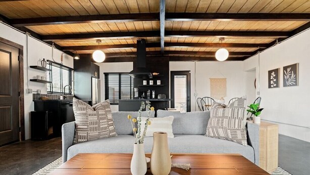 A modern living room with a wooden ceiling, a grey sofa, and a wooden coffee table.