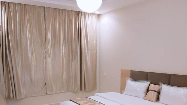 Ein geräumiges Schlafzimmer mit einem großen Bett, einem Kopfteil und einer Deckenleuchte.