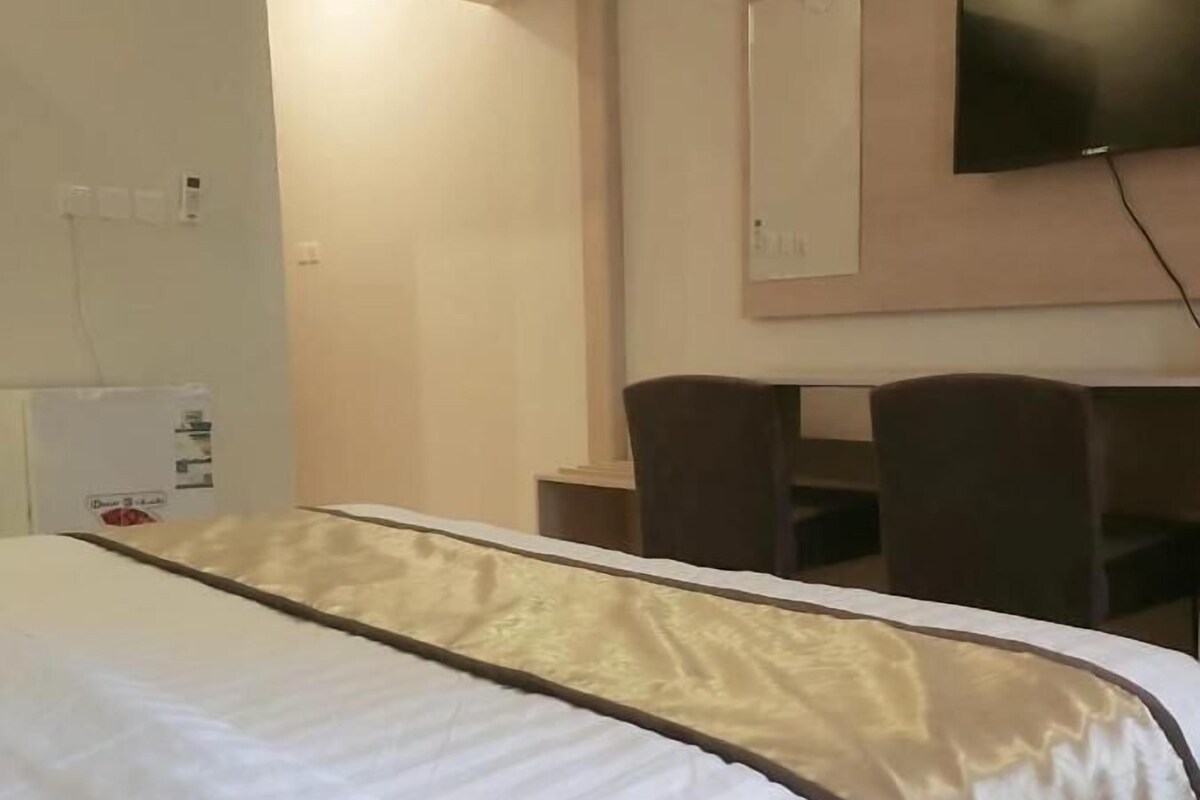 Ein Hotelzimmer mit Bett, Schreibtisch und einem an der Wand befestigten Fernseher.