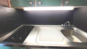 Una cocina compacta con un lavamanos de acero inoxidable, una hornilla integrada y una sola lámpara colgante.