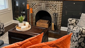 Una sala de estar con chimenea, un televisor montado encima y una zona de estar acogedora con cojines anaranjados.