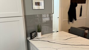 Una cocina con armarios blancos, encimera de mármol y una planta en maceta. Hay dos cuadros en la pared y un letrero que dice 'COFFEE es mi verdadero amor'.