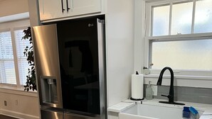 Una cocina moderna con electrodomésticos de acero inoxidable, armarios blancos, un lavamanos integrado y un ventanal con vidrio esmerilado.