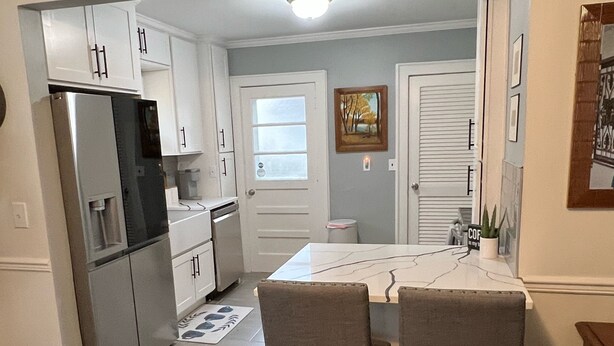Una cocina compacta con armarios blancos, un refrigerador, una mesa de comedor con sillas y una pequeña isla.
