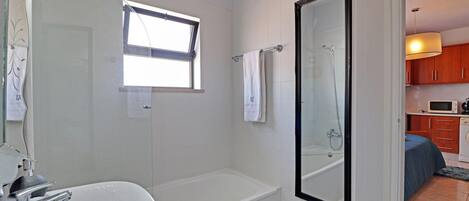 A bathroom with a bathtub, a shower, a sink, and a window.