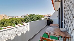 Un balcone con un tavolo e sedie di legno, una pianta in vaso e vista su una zona residenziale con alberi e case.