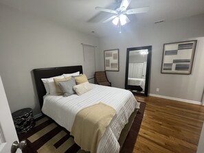 Ein Schlafzimmer mit einem Bett, Deckenventilator, Spiegel und Holzboden.