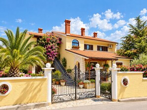 A Mediterranean-style villa with a tiled roof, a stone staircase, and a gated entrance.