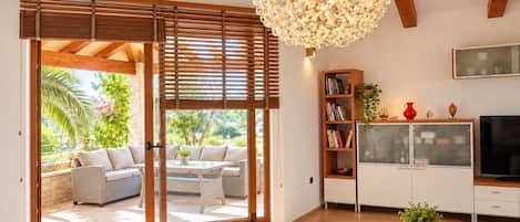 Un salon moderne doté d’une grande porte-fenêtre coulissante donnant sur une terrasse extérieure, d’un plafond en bois et d’un grand luminaire décoratif.