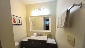 Un baño con inodoro, tocador de madera oscura, lavamanos blanco y espejo sobre el lavamanos.