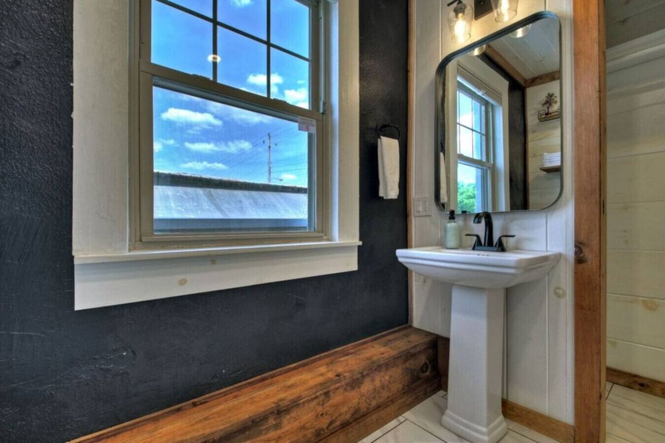 Une salle de bain avec une grande fenêtre, un lavabo blanc et un banc en bois.