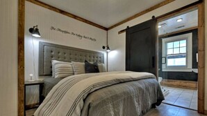 Ein Schlafzimmer mit einem großen Bett, einem hölzernen Kopfteil, einer Wandlampe und einer Schiebetür zum Badezimmer.