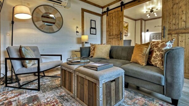 Ein gemütliches Wohnzimmer mit einer grauen Couch, einem Holztisch und einem gemusterten Teppich.