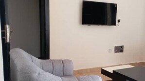 Una stanza con un divano grigio, una televisione a schermo piatto montata a parete e un tavolino.