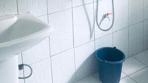 Un bagno con un lavandino bianco, un secchio blu e un tubo doccia.