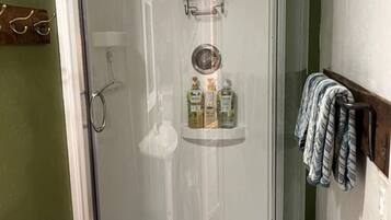 Ducha con mampara de vidrio y estante integrado para artículos de aseo.