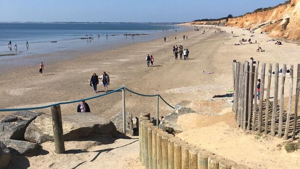 A sandy beach with people walking and sunbathing, wooden structures, and a clear blue sky.