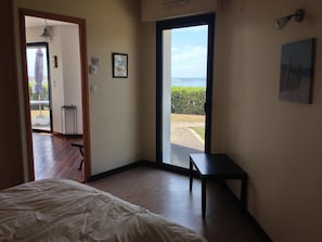Un dormitorio con cama, una mesita y vista al exterior por un ventanal corredero.