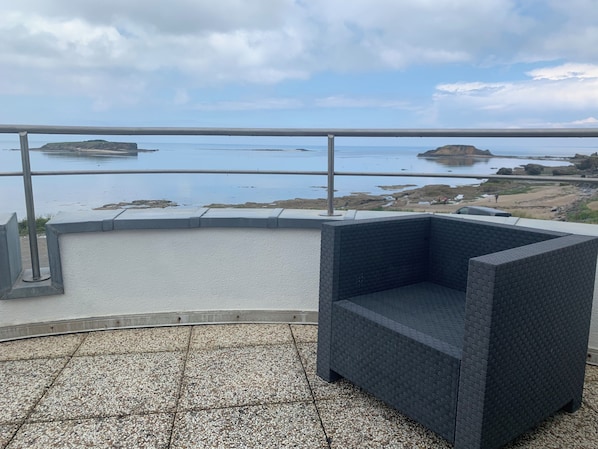 A balcony with a view of rocky coastline and calm sea.