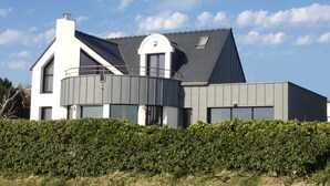 A modern house with a prominent balcony, a large window, and a well-maintained hedge in front.