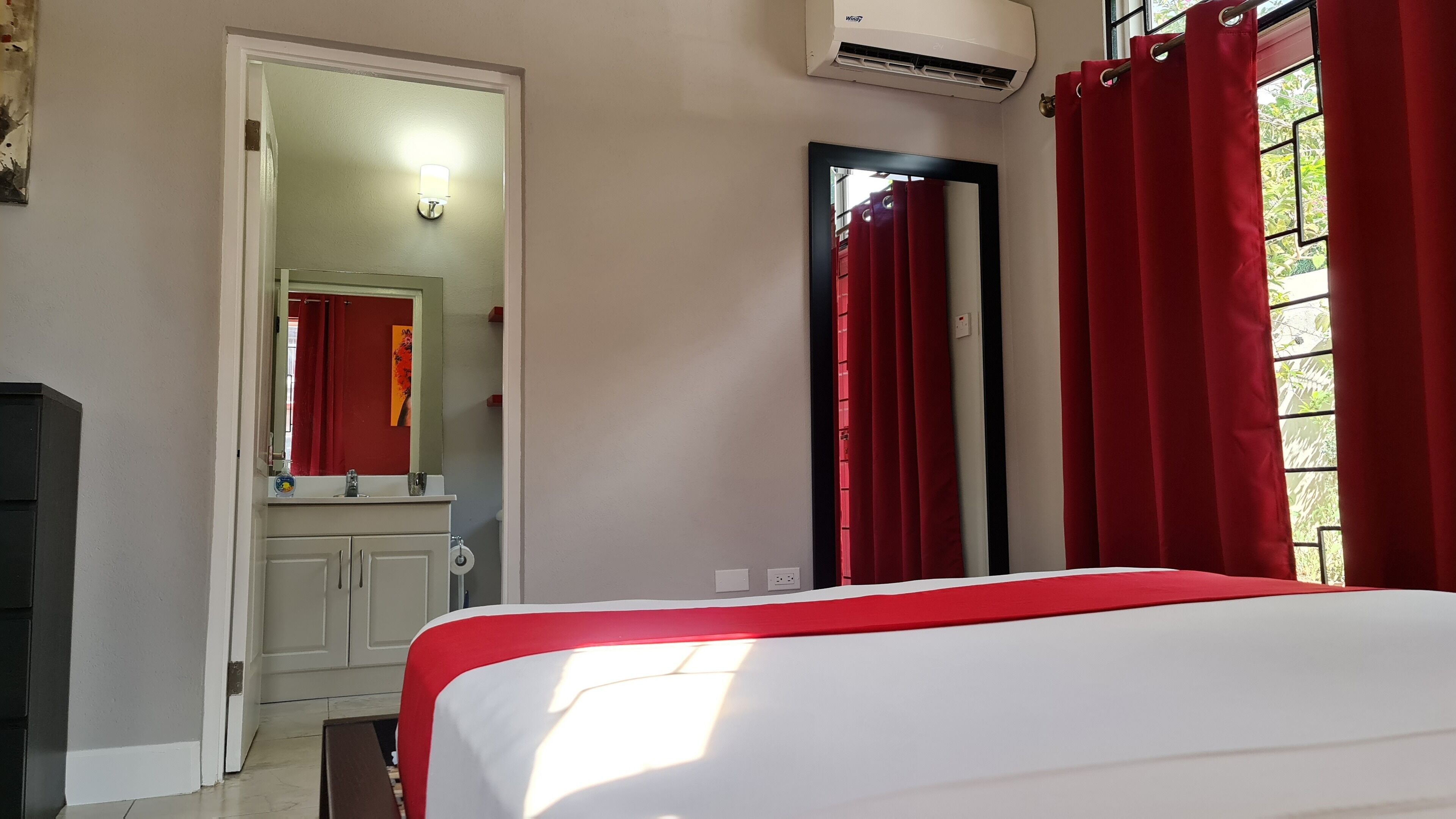 Une chambre à coucher avec un lit, une salle de bain avec un miroir et des rideaux rouges.