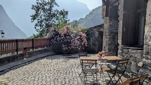 Un edificio de piedra con balcón, asientos al aire libre y vista a las montañas.