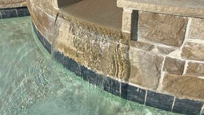 Una piscina de piedra con agua cristalina, rodeada por una terraza de piedra y una valla de madera.