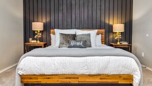 Una cama bien tendida con cabecera de madera, dos mesitas de noche con lámparas y una almohada con la palabra “blessed”.