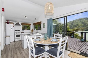 Une cuisine moderne avec des appareils électroménagers blancs, un coin repas avec de la vaisselle bleue et blanche, et une terrasse offrant une vue sur un lac et une forêt.