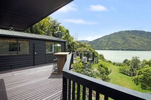 Une maison moderne dotée d’une terrasse offrant une vue sur un lac et des collines.