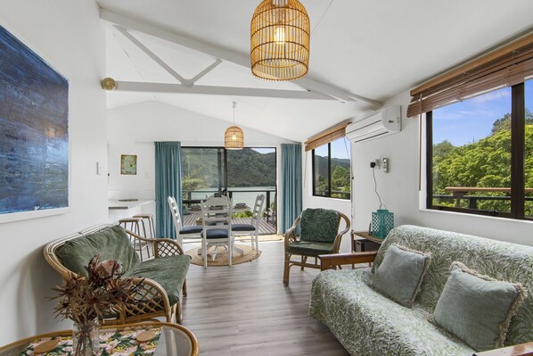 Um quarto espaçoso com uma grande janela que oferece vista para uma paisagem exuberante, uma área de jantar com mesa e cadeiras, e um espaço de estar acolhedor com um sofá e poltronas.