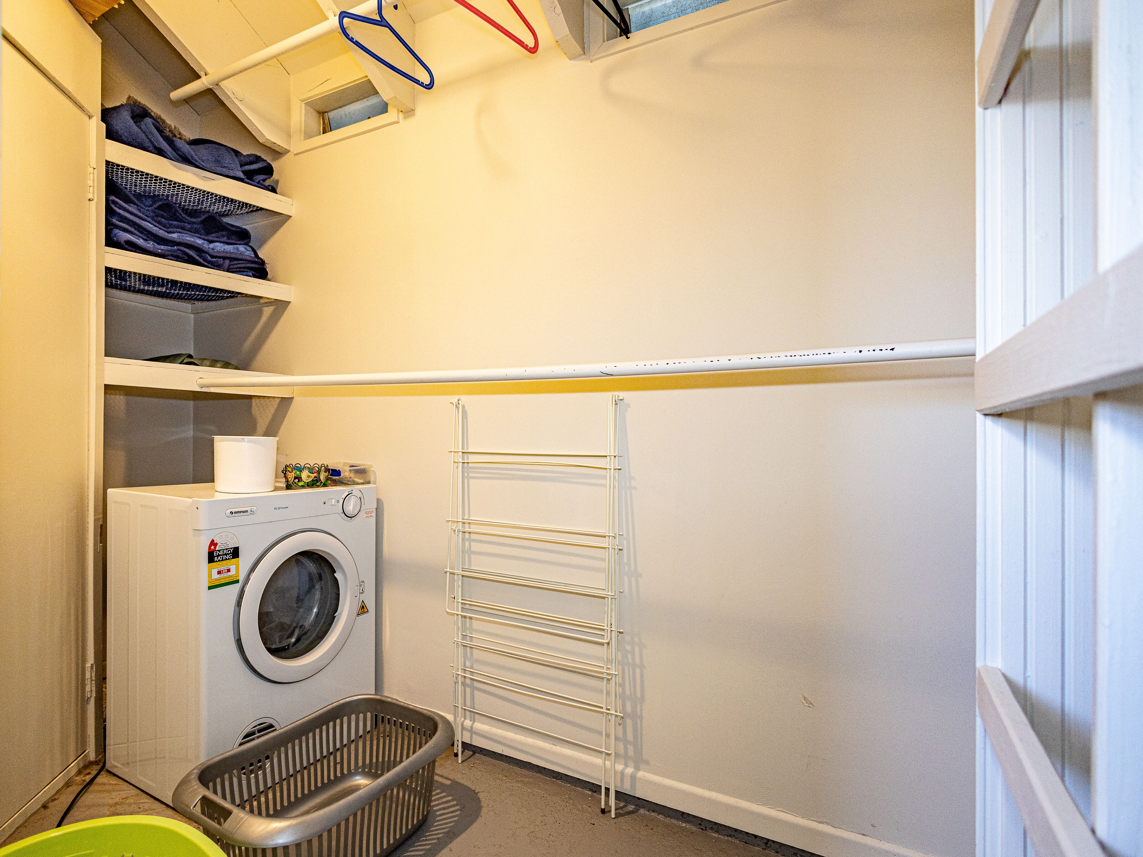 A laundry room with a washing machine, a drying rack, and shelves with folded clothes.