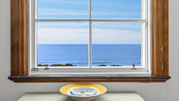 A window with a view of the ocean, a wooden window frame, and a small table with a bowl. - The Professor's Beach House - Brighton Home (Dunedin)