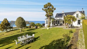 A house with a large lawn, a dining area, and a view of the sea. - The Professor's Beach House - Brighton Home (Dunedin)