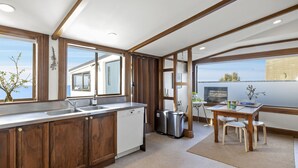 A modern kitchen with wooden cabinets, a built-in dishwasher, and a dining area with a table and chairs. - The Professor's Beach House - Brighton Home (Dunedin)
