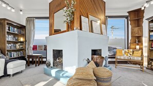 A modern living room with a fireplace, bookshelves, a sofa, and a dining area. - The Professor's Beach House - Brighton Home (Dunedin)