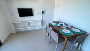 Ein Essbereich mit einem für vier Personen gedeckten Tisch, einem an der Wand montierten Flachbildfernseher und einer Tür mit Griff.