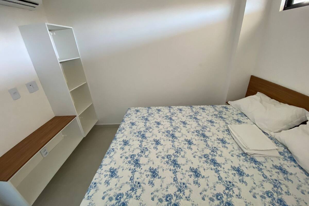 A bedroom with a bed, white walls, a wooden headboard, and a white wardrobe.