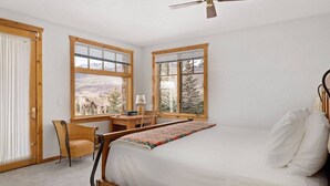 A bedroom with a bed, a desk, and a chair. There are large windows with mountain views. - Fairway Vista: Massive Mountain Views w/ hot tub! (Mountain Village)